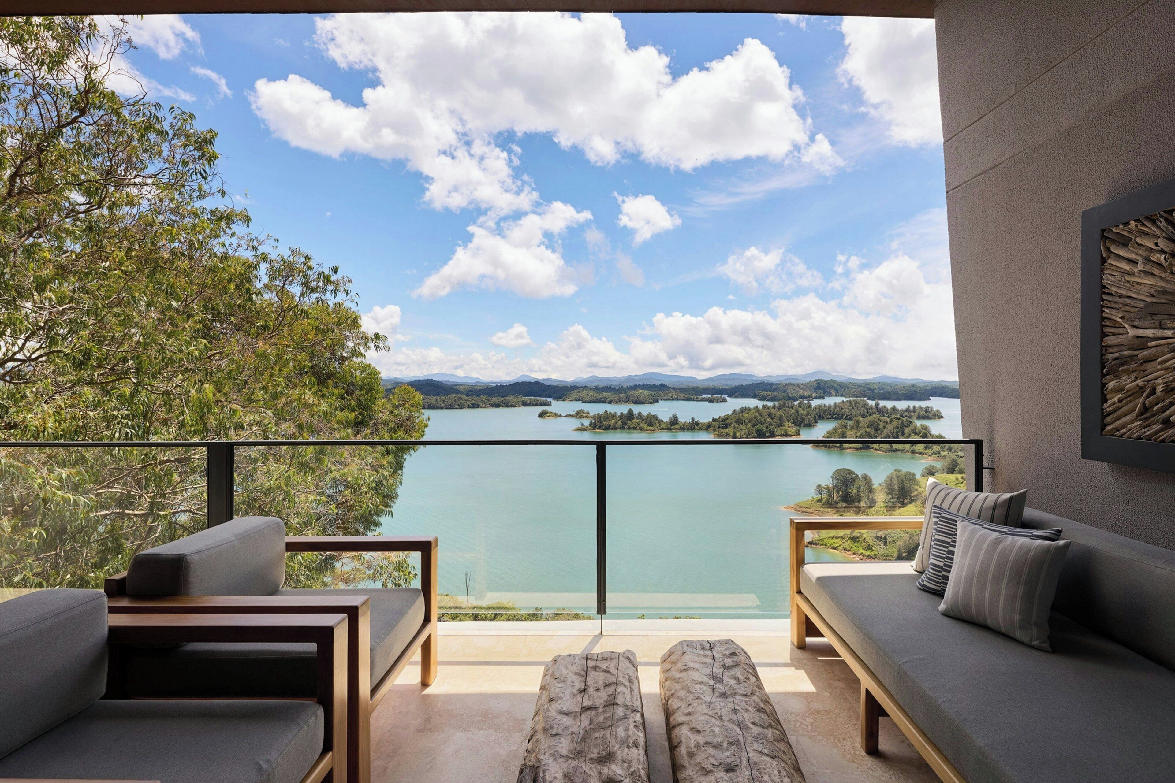 Un balcon avec vue sur un lac et des montagnes, aménagé avec un canapé et un banc.