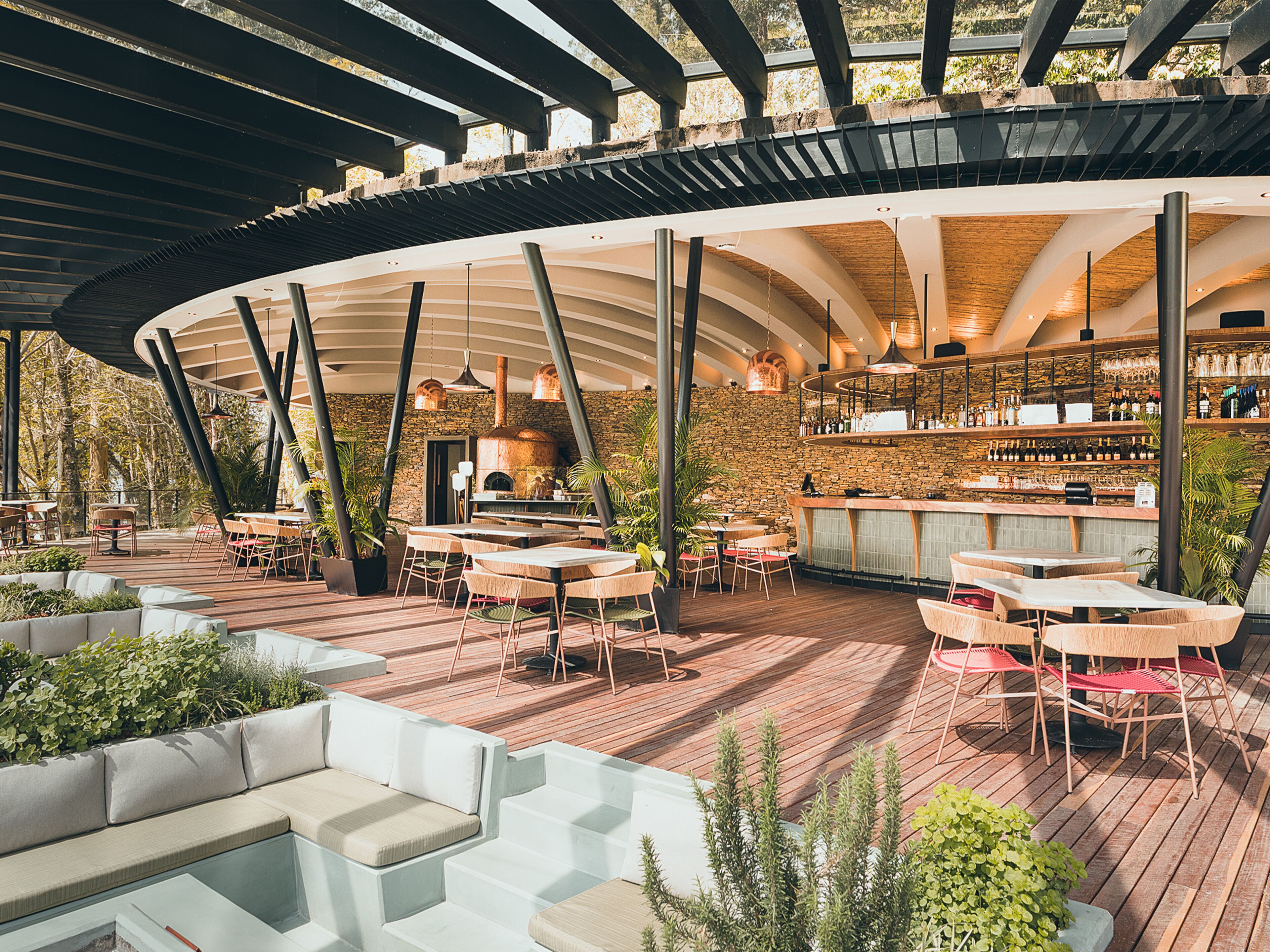 An outdoor dining area with wooden tables and chairs, a stone wall, and a bar with a rustic wooden counter.