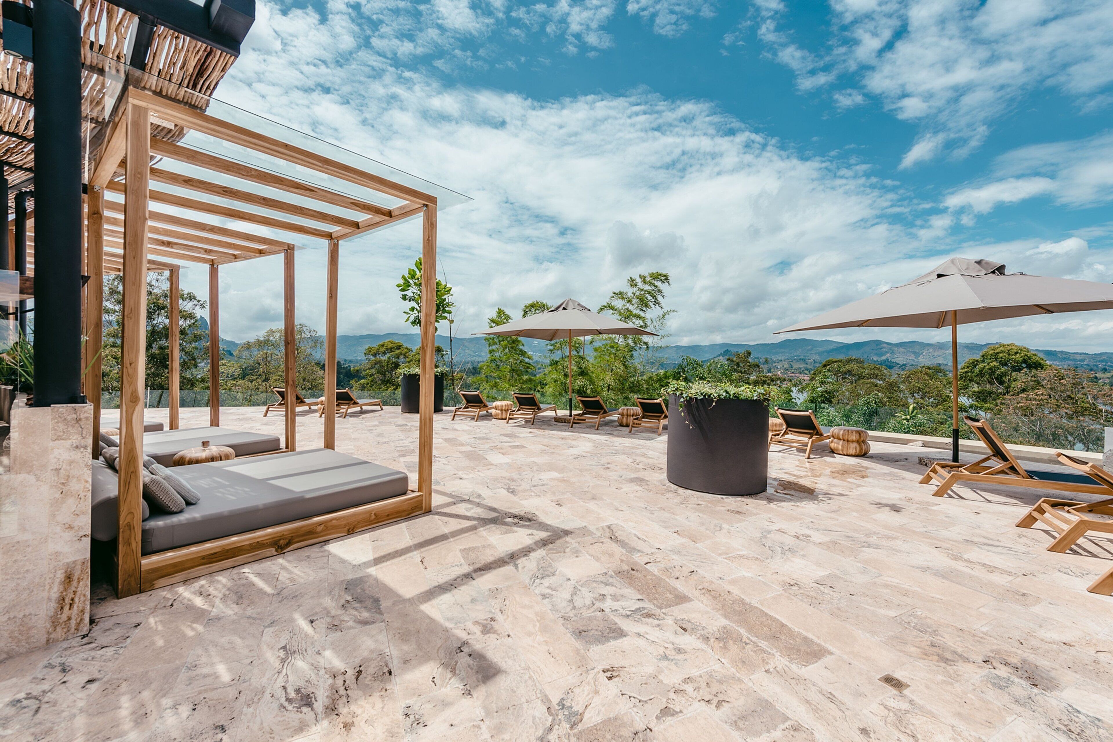 A rooftop terrace with wooden loungers, a pergola, and umbrellas.