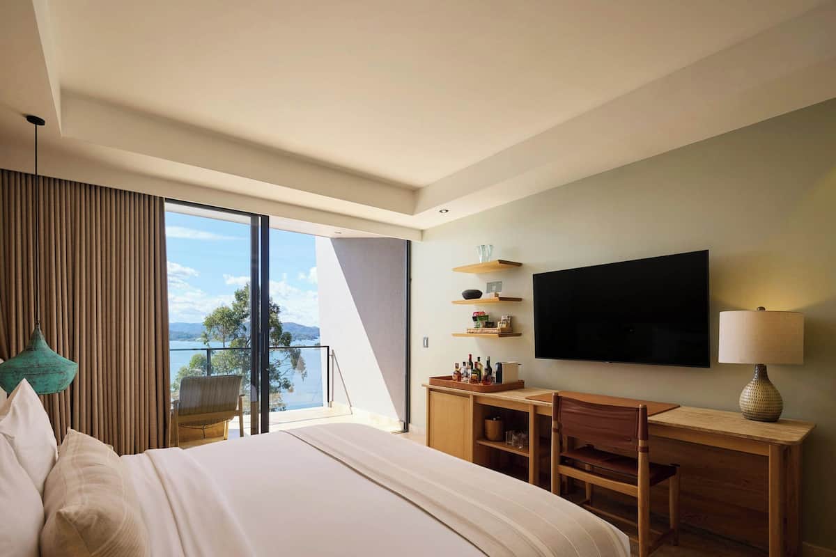 Habitación de hotel con una cama grande, un escritorio, un televisor y un balcón con vista al mar.