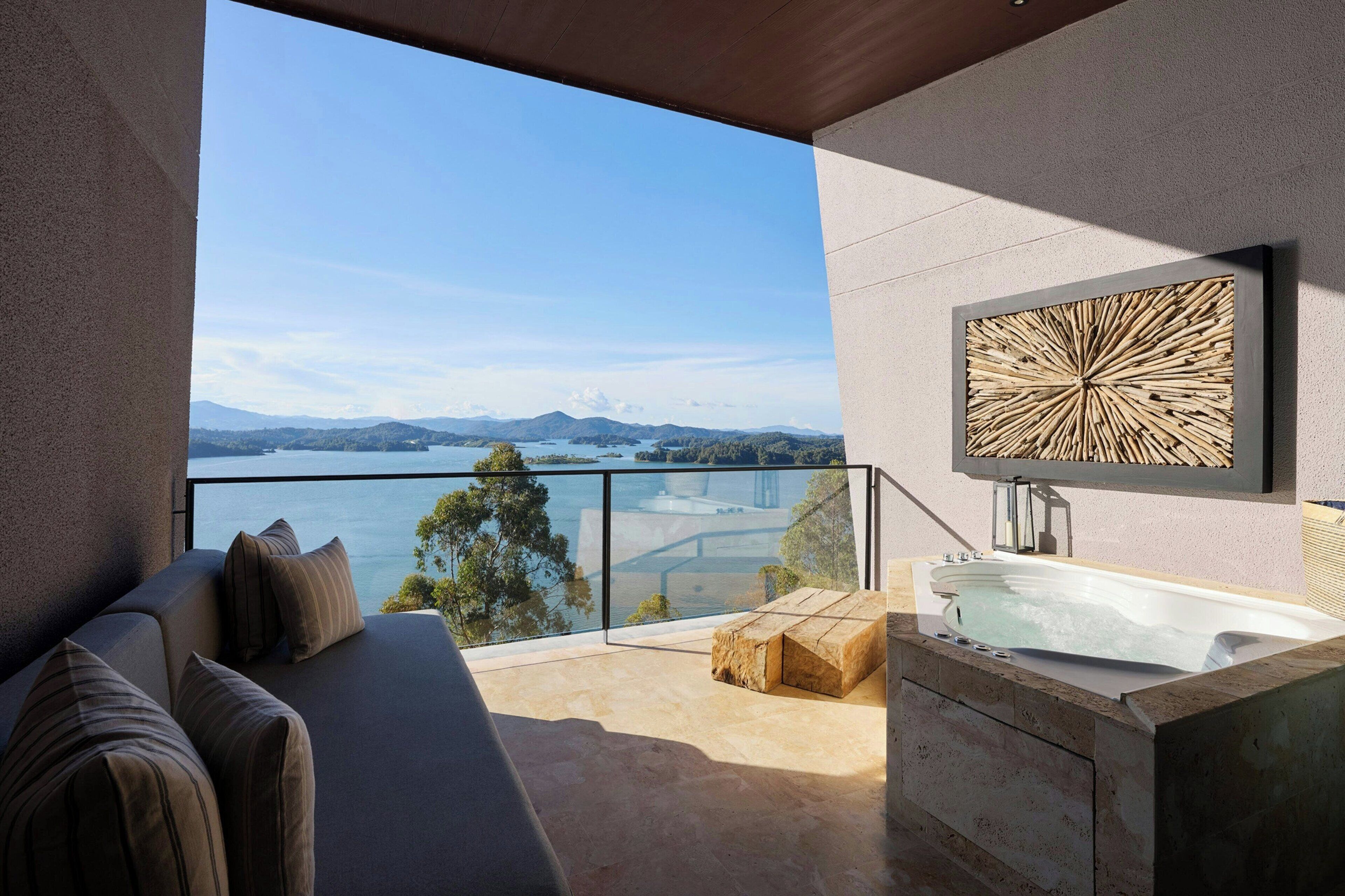 Ein Balkon mit Blick auf einen See und Berge, ein Sofa, ein hölzerner Hocker und eine Badewanne.