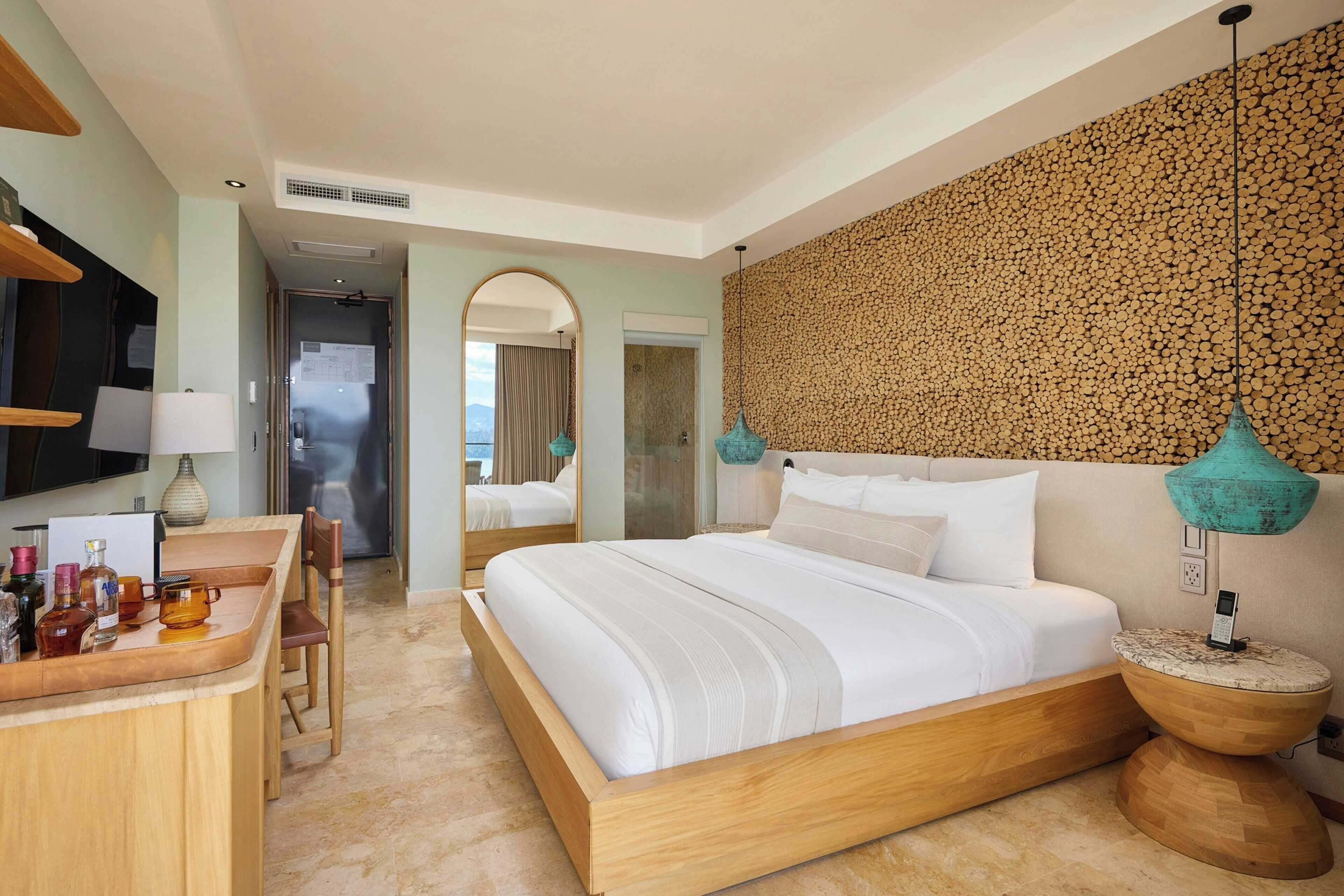 A hotel room with a large bed, a wooden desk, a mirror, and a wall with a textured pattern.