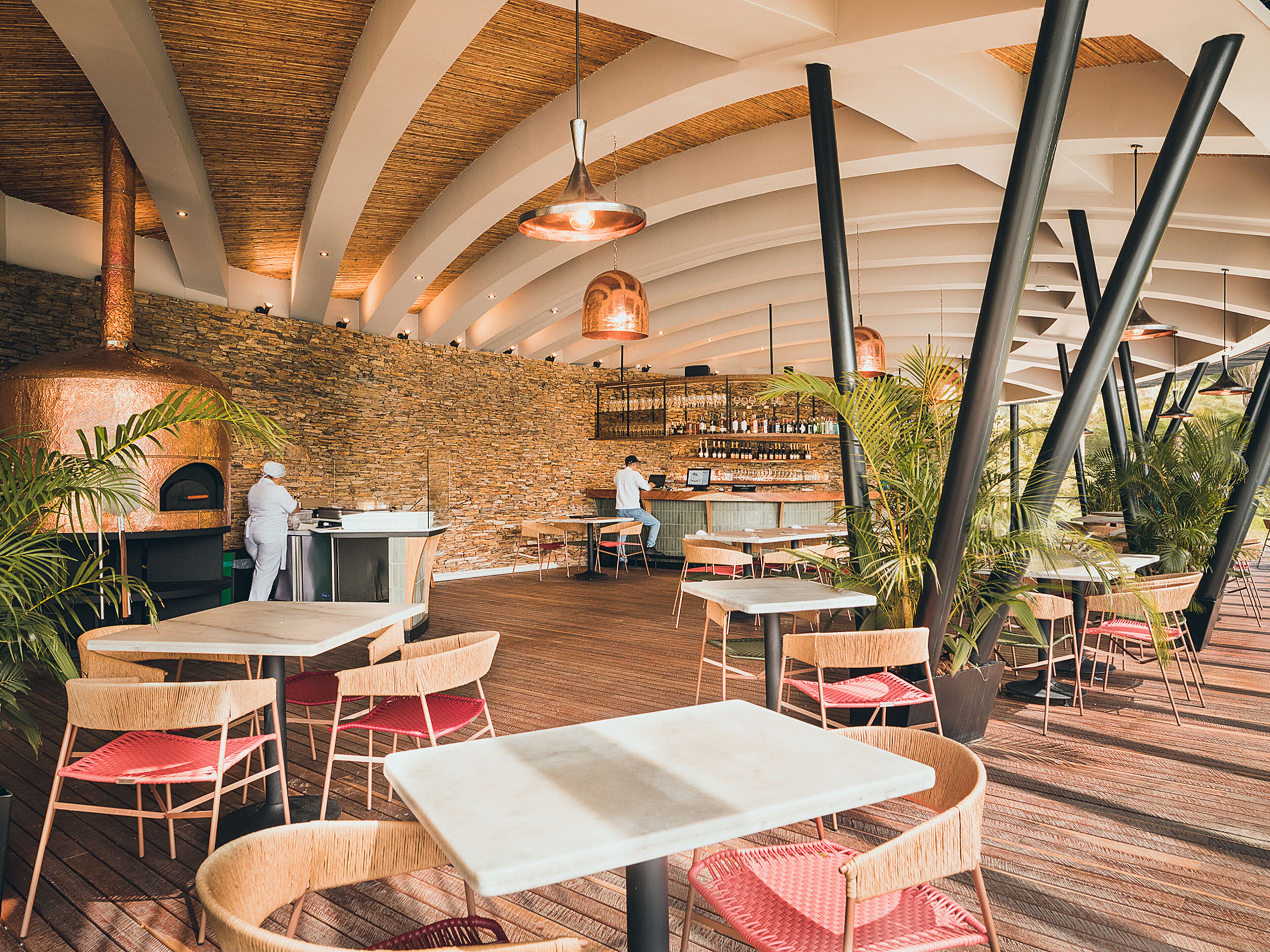 Un restaurante con pared de piedra, techo de madera y mesas con sillas de mimbre.
