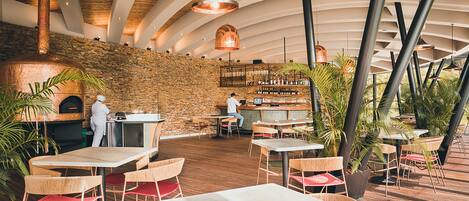 Un restaurante con pared de piedra, techo de madera y mesas con sillas de mimbre.