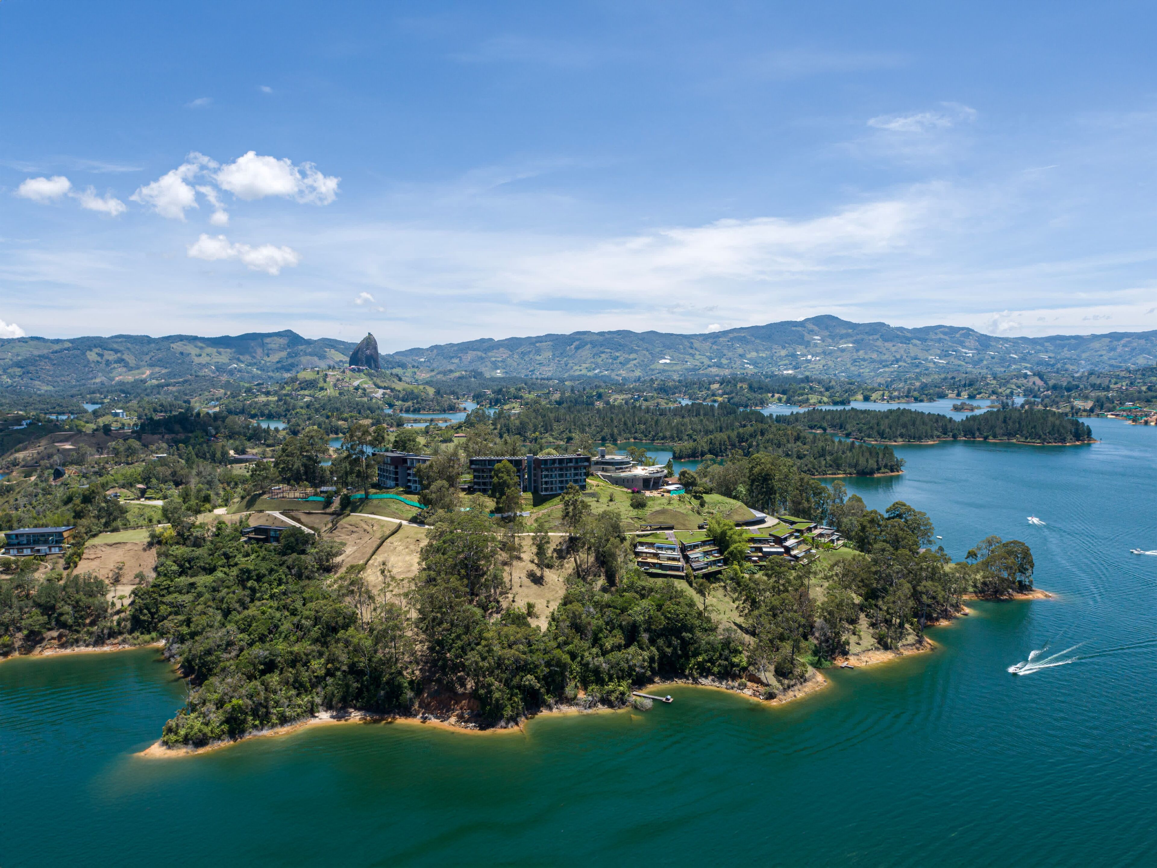 An aerial view of a coastal area with buildings, a lake, and surrounding hills.