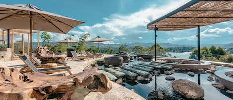 Un espace piscine agrémenté de chaises longues et de parasols, entouré de formations rocheuses naturelles et offrant une vue sur les montagnes lointaines.