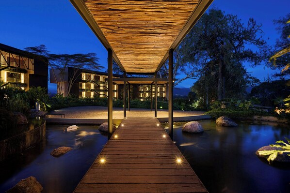 Una terraza de madera que conduce a un espacio cubierto con vista a un cuerpo de agua tranquilo y vegetación circundante.