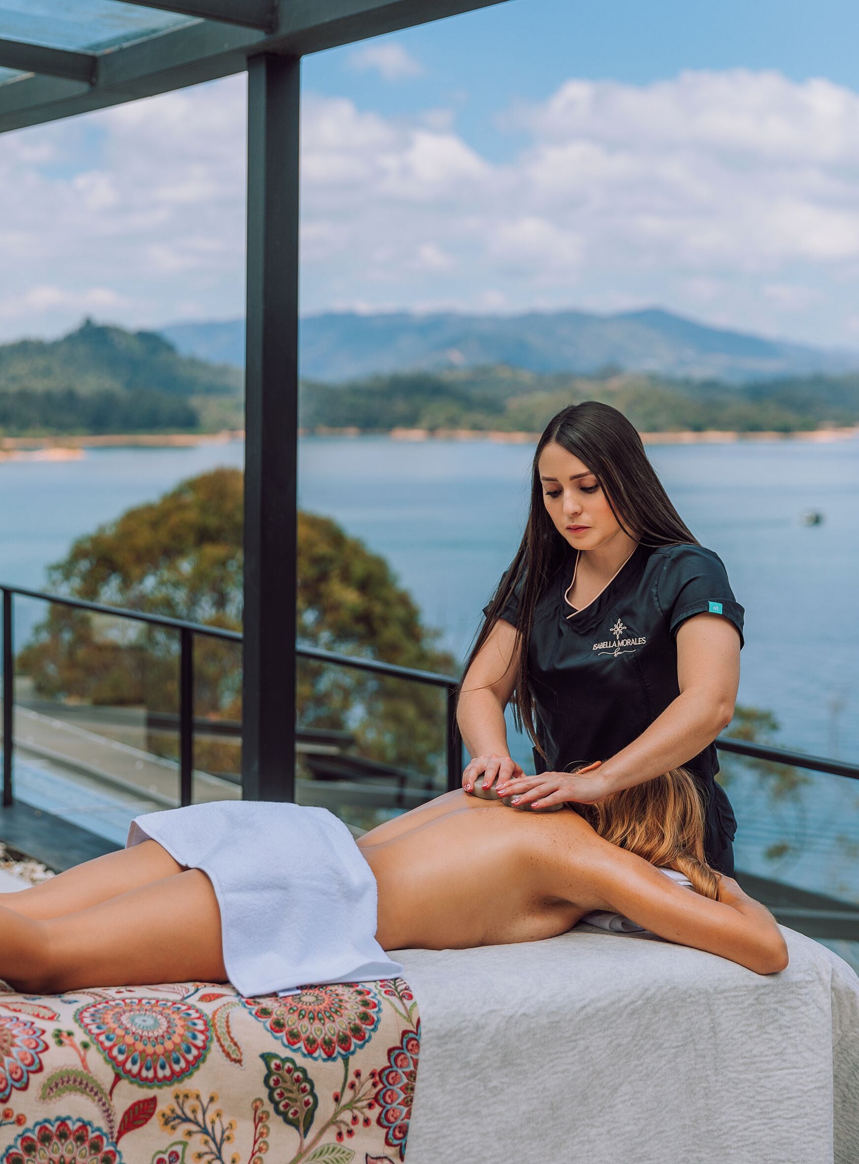 Sesión de masoterapia en un balcón con vistas panorámicas a un lago y montañas.