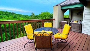 A wooden deck with a round table and four chairs, surrounded by lush greenery and a clear sky. - 2BR Condo Near SDC | Lake Views (Branson)