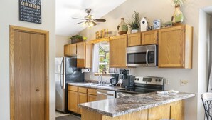 A kitchen with wooden cabinets, a granite countertop, a refrigerator, a microwave, an oven, and a ceiling fan. - 2BR Condo Near SDC | Lake Views (Branson)