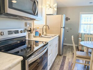 A kitchen with a stove, microwave, refrigerator, and a dining area with a table and chairs.