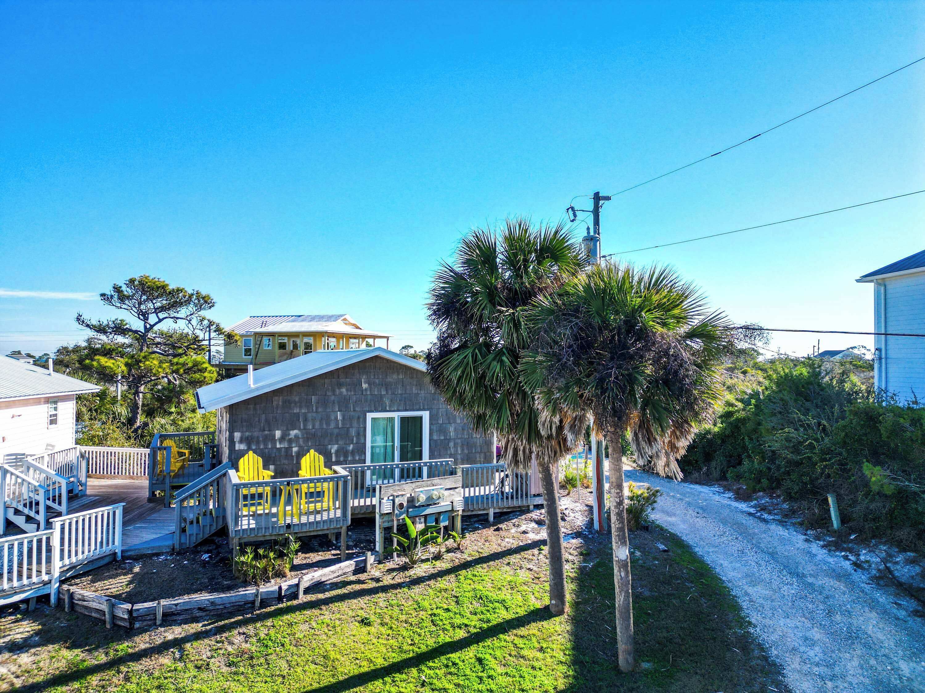 A beachfront property with a wooden cabin, a covered deck with yellow chairs, and a gravel path.