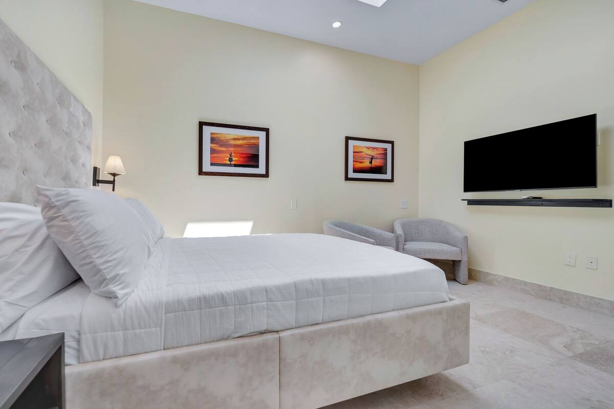 Un dormitorio moderno con una cama grande, un televisor de pantalla plana en la pared y dos cuadros enmarcados.