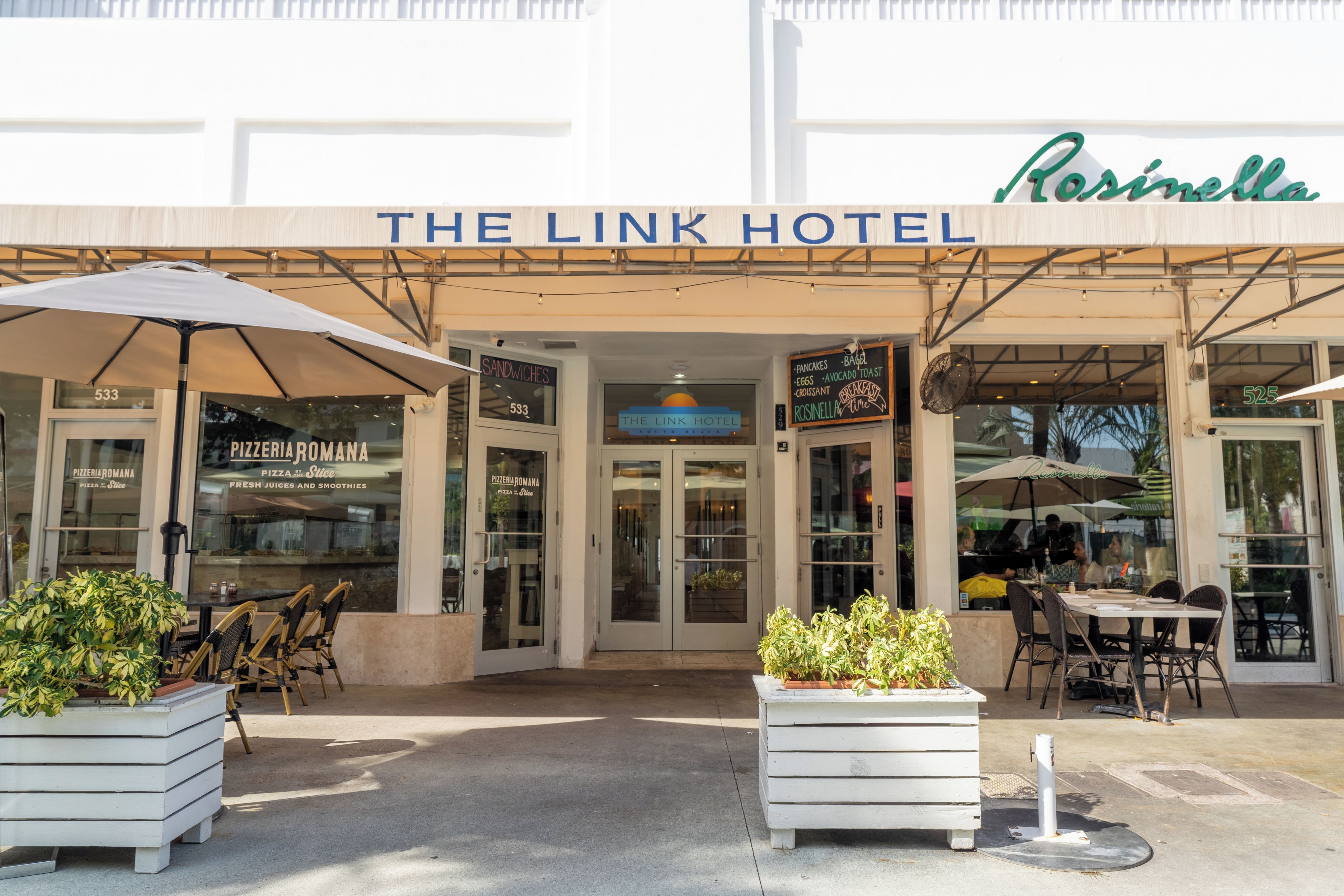 The exterior of The Link Hotel with a signboard, potted plants, and outdoor seating.