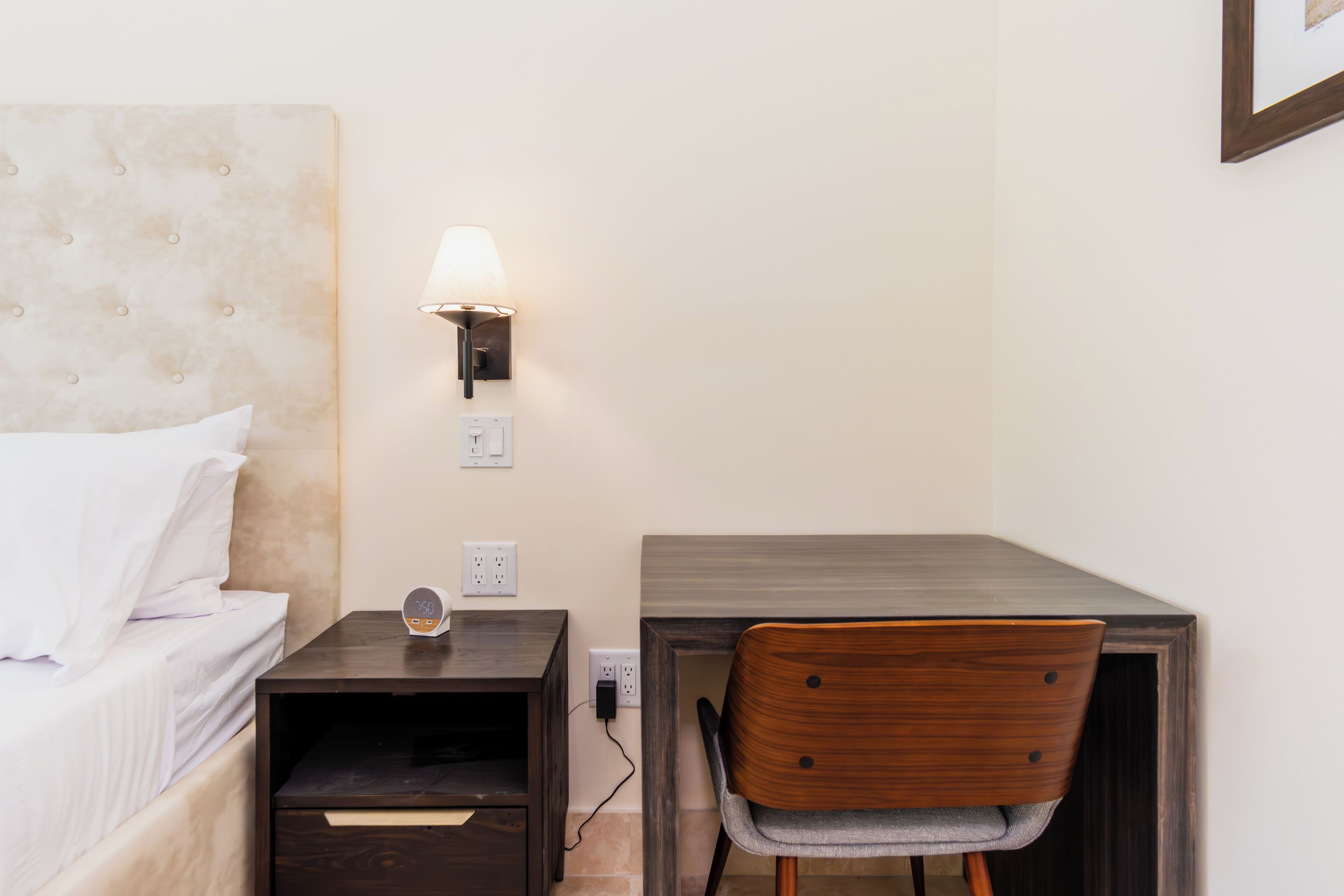 Un dormitorio con cama, mesita de noche, lámpara y escritorio con silla.