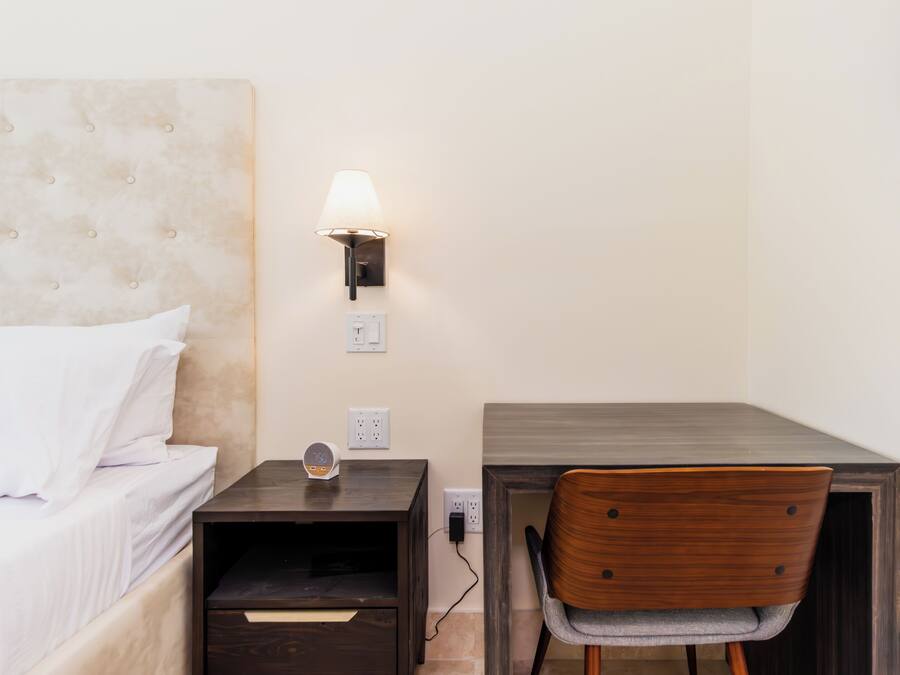 Un dormitorio con cama, mesita de noche, lámpara y escritorio con silla.