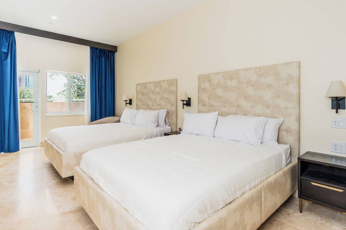Habitación de hotel con dos camas, una mesita de noche y una lámpara.