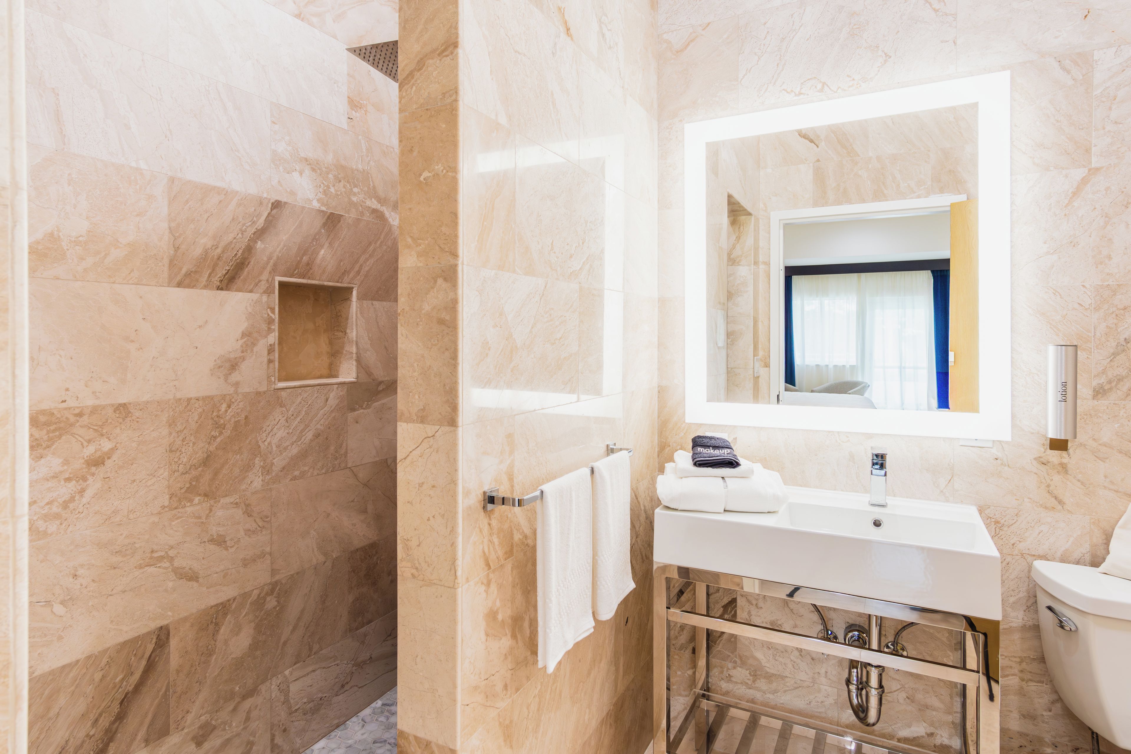 A bathroom with a marble wall, a sink with a mirror, a toilet, and a shower area.