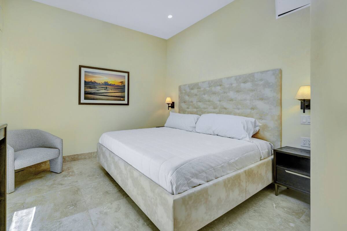 Una habitación de hotel con una cama, una silla, un escritorio, un cuadro y una lámpara.