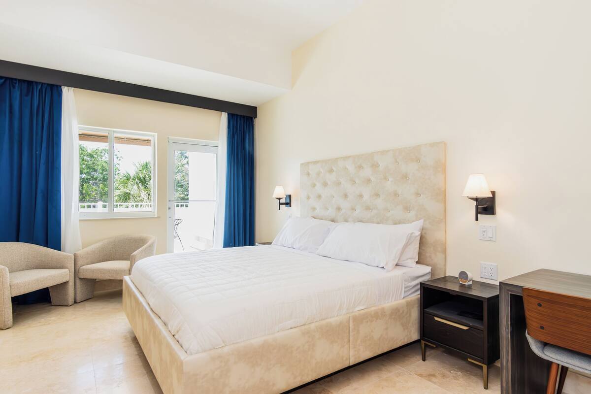 Un dormitorio con una cama grande, una silla, un escritorio y una ventana con cortinas.