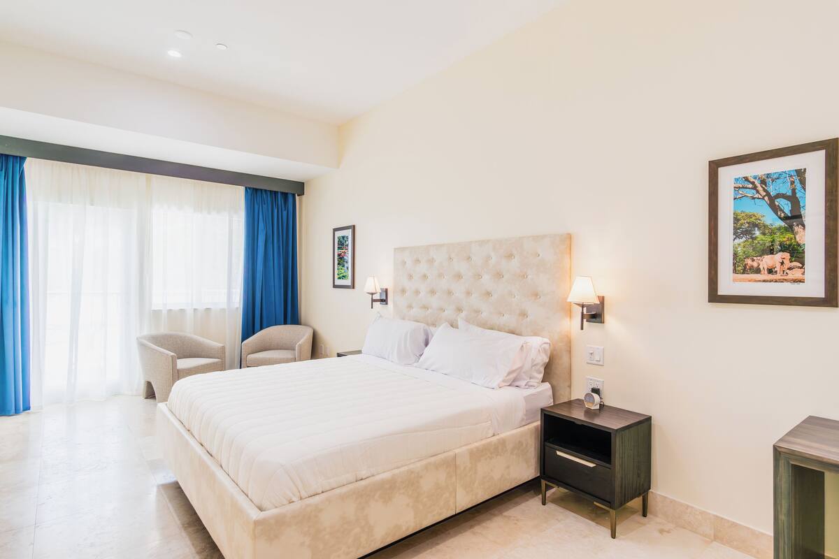 Habitación de hotel con una cama grande, una mesita de noche, una silla y un cuadro en la pared.