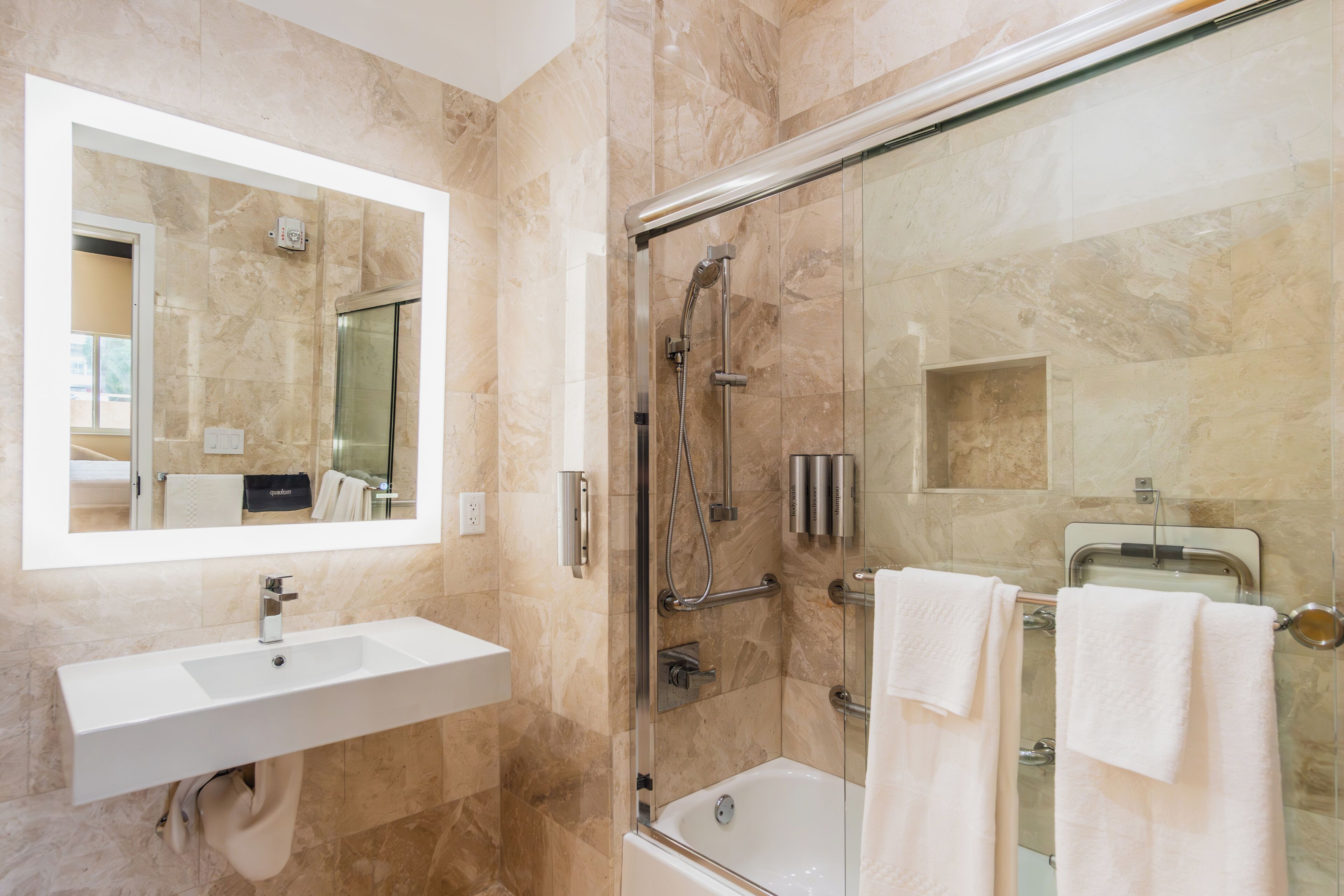 A modern bathroom with a marble sink, a glass-enclosed shower, and two white towels.