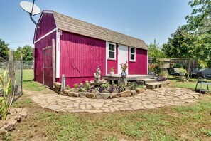 A red barn with a satellite dish, a stone pathway, and a small garden with plants and a statue.
