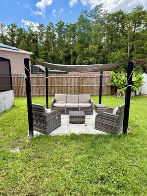 Un espace extérieur aménagé en terrasse, avec des sièges confortables, une petite table et une structure en forme de pergola.