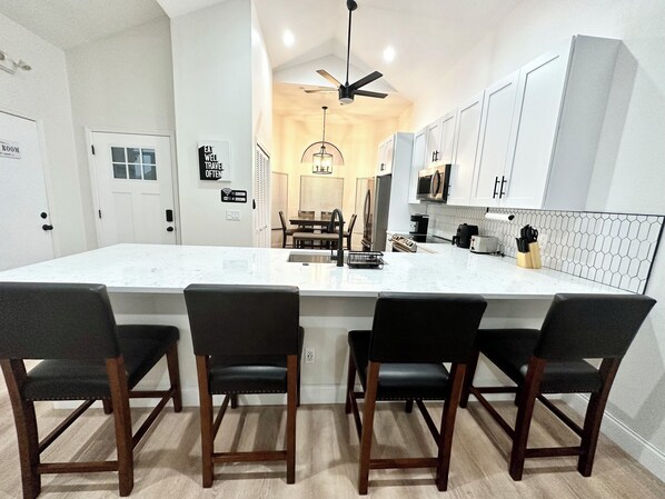A modern kitchen with a large island, white cabinetry, and a dining area with four chairs.