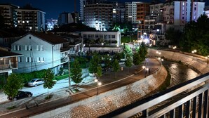A nighttime cityscape with a curved road, buildings, and a stone wall. - Premium Apartments (Gjakova)