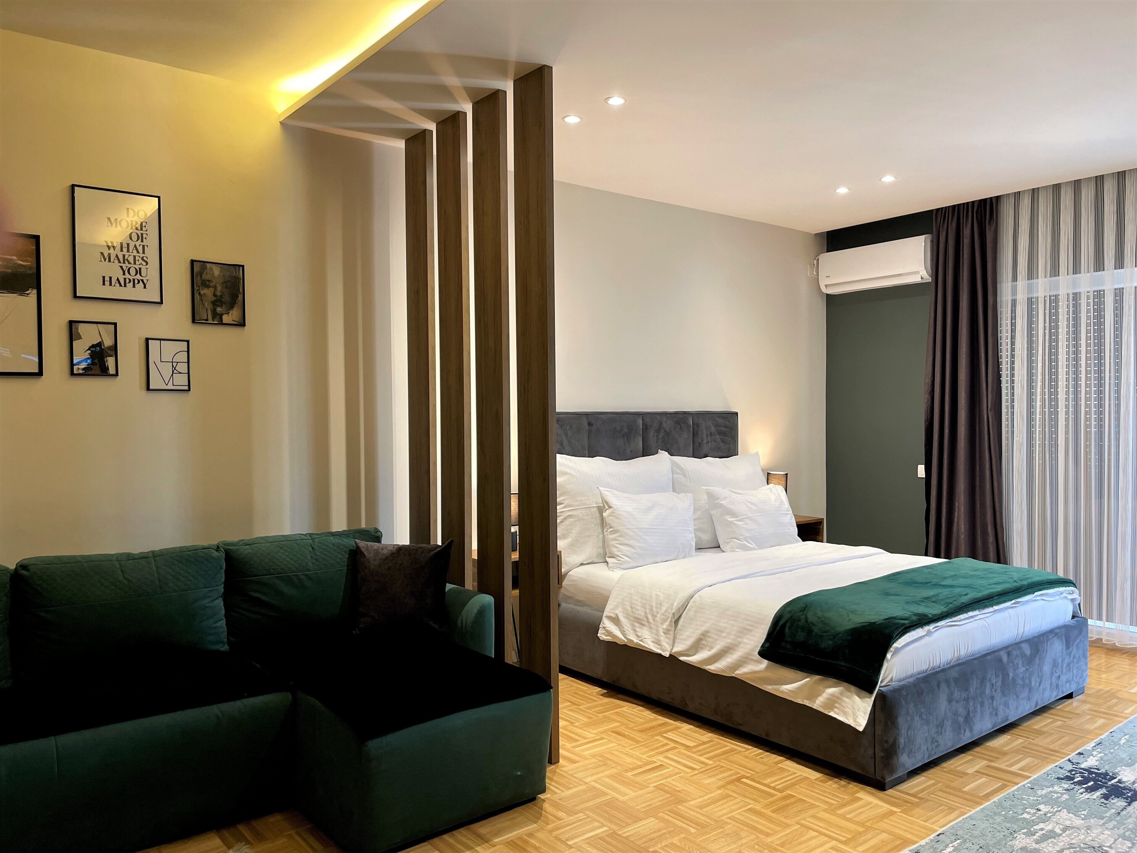 Un dormitorio moderno con cama, sofá verde y separador de madera.