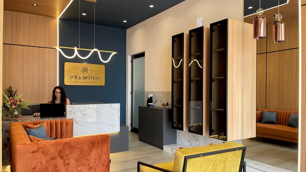 A modern hotel reception area with a receptionist, a marble reception desk, and a seating area with orange and yellow chairs. - Premium Apartments (Gjakova)