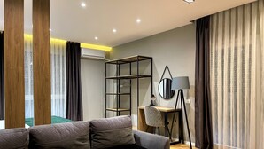 A modern living room with a sofa, a small round table, a desk with a lamp, and a wardrobe. - Premium Apartments (Gjakova)