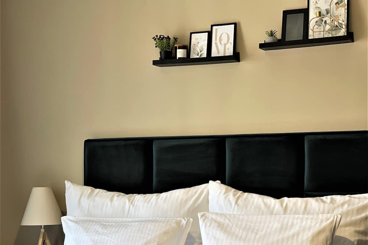Un lit bien fait, avec une literie blanche et un plaid marron, une tête de lit noire et une table de chevet avec une lampe.