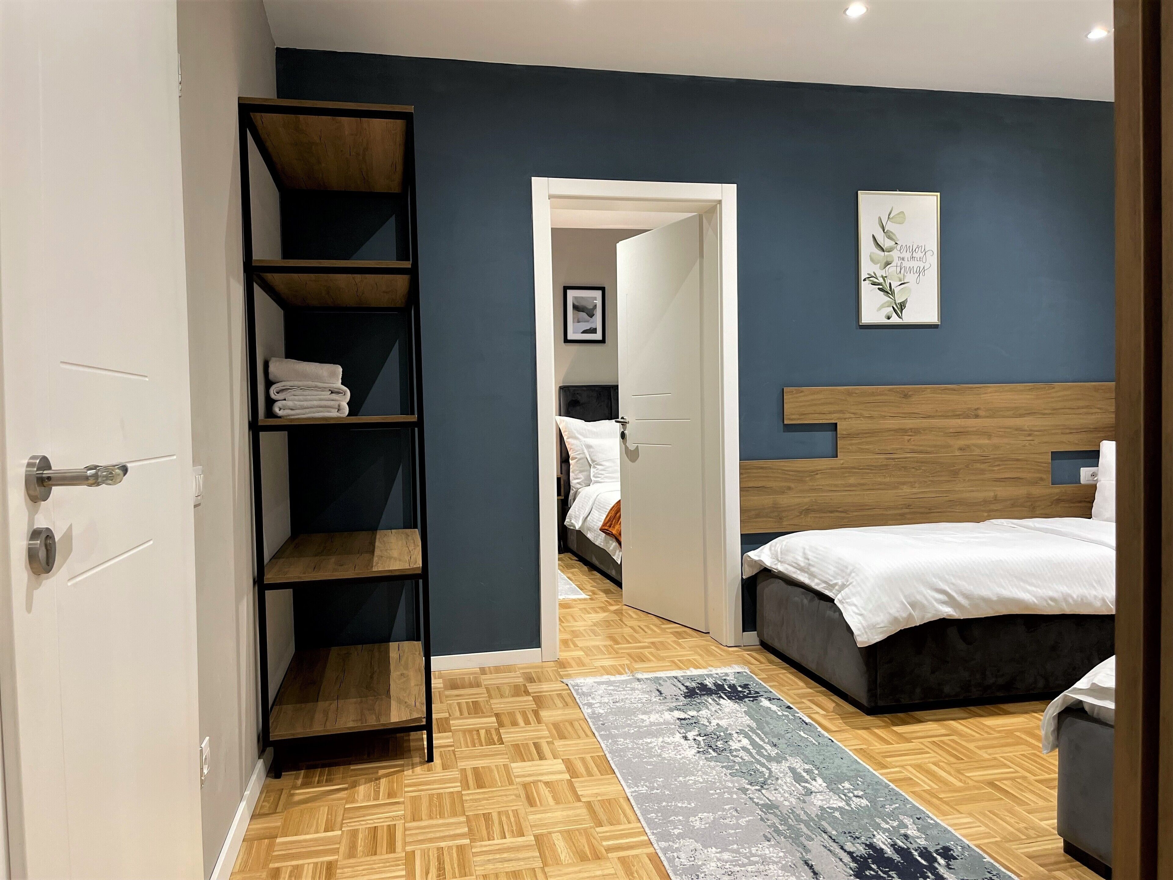 Un dormitorio moderno con cabecera de madera, una cama grande, un armario empotrado y un pasillo que conduce a otra habitación.