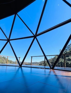 A spacious, open interior with a geometric metal framework and a clear view of a bridge and hills in the background. - Chales Cabana (Camanducaia)
