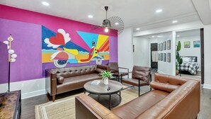 A modern living room with a vibrant mural, leather sofas, a round coffee table, and a ceiling fan. - Blue Lagoon Spanish Retreat 5BRs and Pool Airport (Houston)