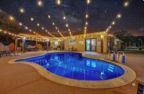 A swimming pool with a curved edge, surrounded by a covered patio area with string lights overhead.