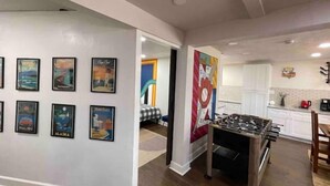 A living room with a foosball table, a kitchen with white cabinets, and a wall with framed travel posters. - Blue Lagoon Spanish Retreat 5BRs and Pool Airport (Houston)