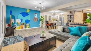 Una sala de estar moderna con un mural colorido, un sofá, una barra de café y un comedor.