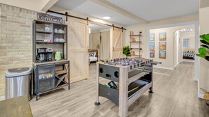 Una habitación acogedora con un bar de café, una mesa de fútbol y una cama con colcha a cuadros.