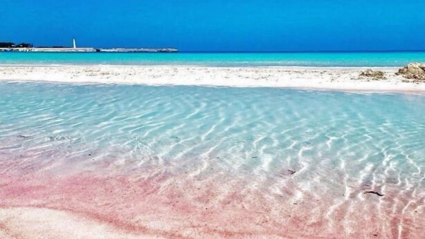 A beach with clear shallow waters, a lighthouse in the distance, and a rocky outcrop. - Gaia Verde by Interhome (San Vito lo Capo)