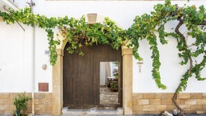 A building entrance with a wooden door, a stone wall, and a vine-covered archway. - Gaia Verde by Interhome (San Vito lo Capo)