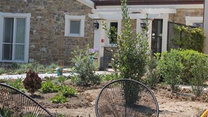 A stone building with a tiled roof, a front porch, and a garden with various plants and a chair. - Tenuta Bellelli (Castellabate)