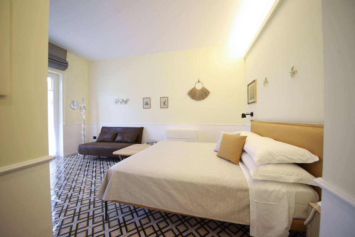 A hotel room with a bed, a sofa, a small table, and a patterned floor.