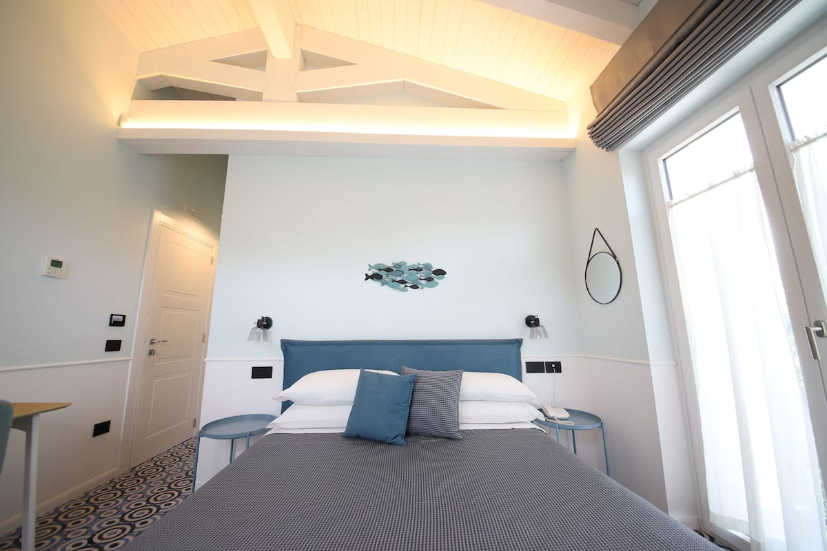 A bedroom with a bed, bedside tables, a wall-mounted lamp, a door, and a window.
