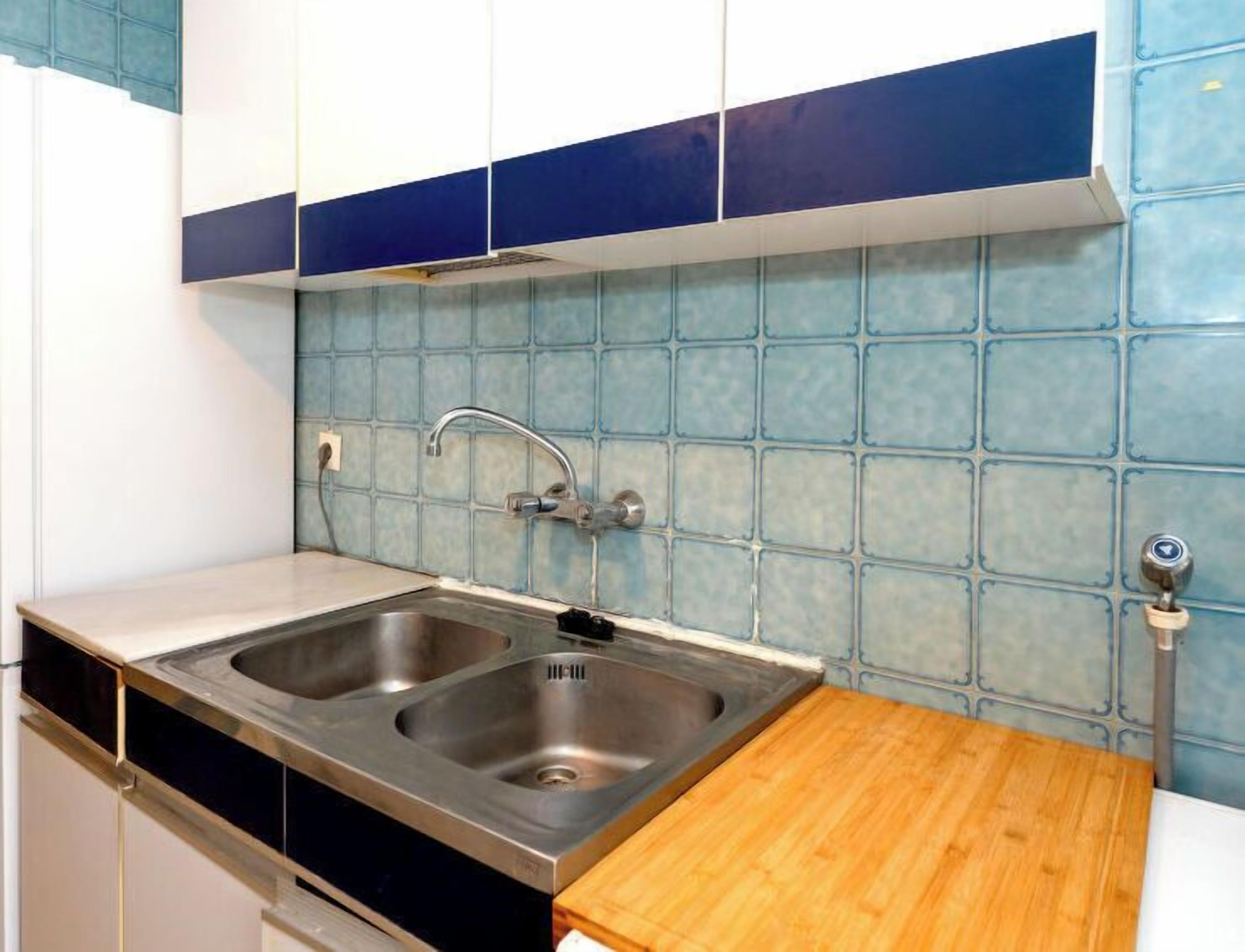 Een keuken met twee roestvrijstalen spoelbakken, een houten aanrechtblad en een blauwe betegelde spatwand.