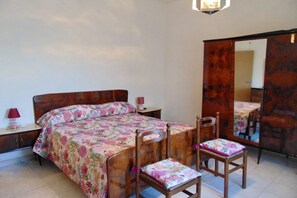 A bedroom with a bed, bedside table, chair, and a large mirror.