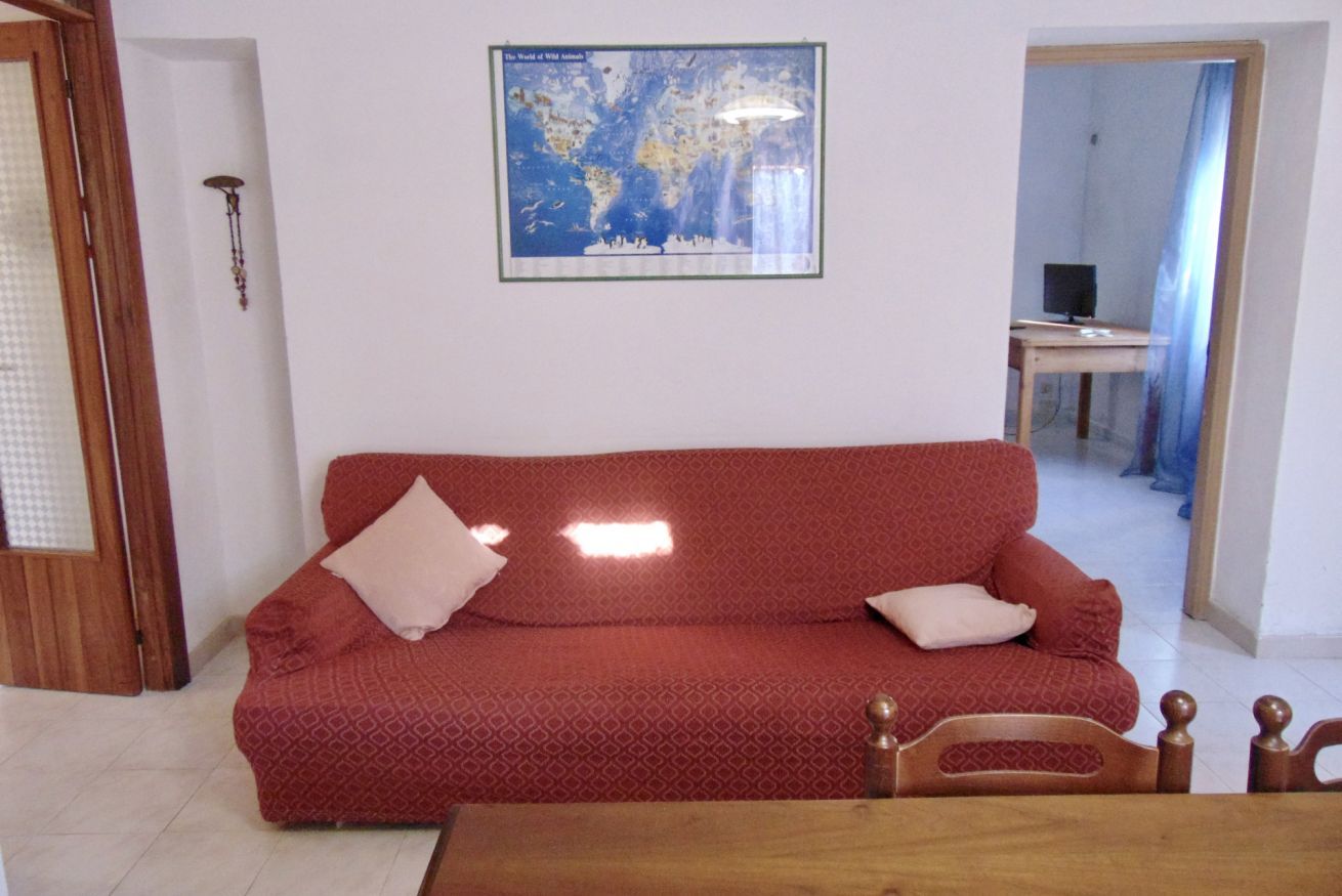 A red patterned sofa with pillows, a wooden chair, a framed world map, and a small table.