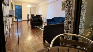 Ett modernt vardagsrum med ett matbord i trä, en blå soffa och en svart fåtölj. Det finns ett soffbord i glas och en hängande lampa.